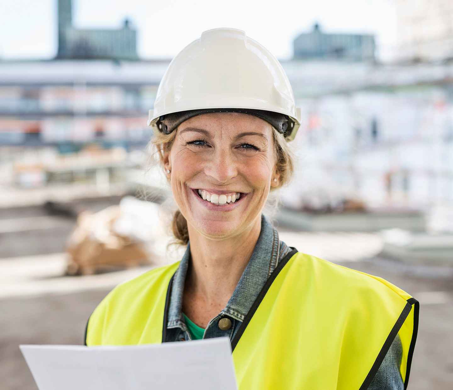 Glad kvinnlig medarbetare med hjälm på byggarbetsplats