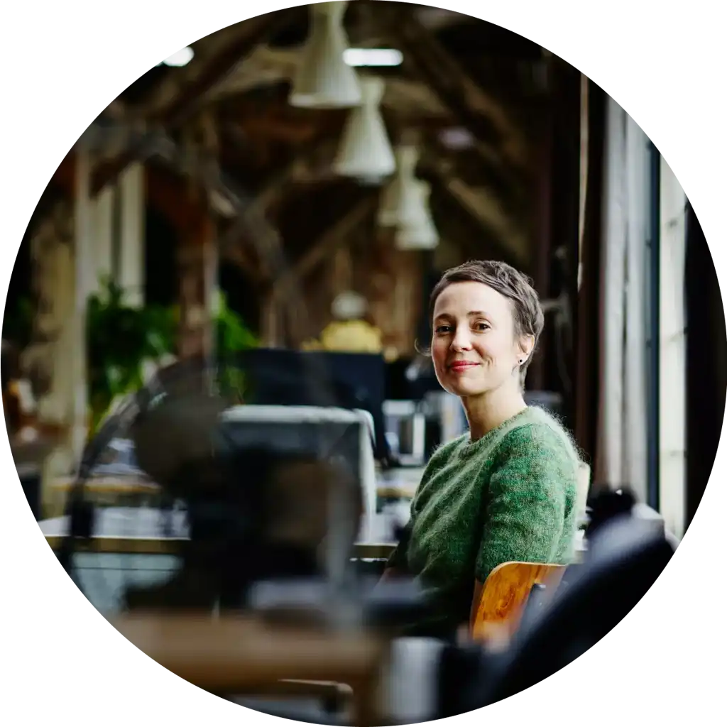 Leende anställd bakom hennes skrivbord i öppet kontorslandskap.