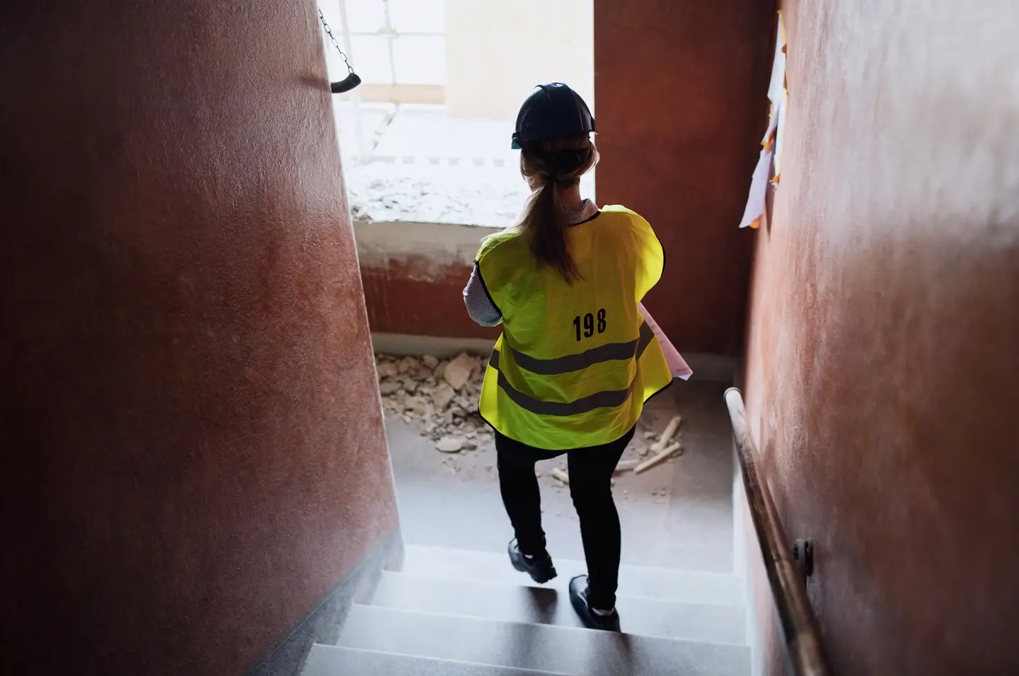 Person med hjälm och reflexväst som går ner för en trappa i en byggnad under renovering.