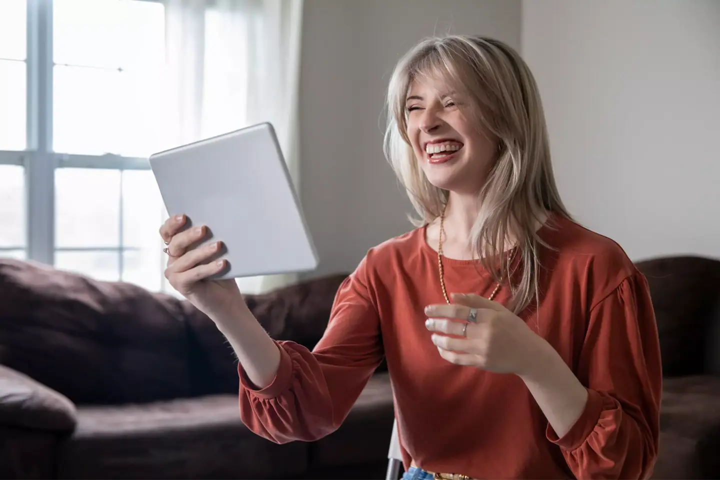 Skrattande kvinna deltar i digitalt möte på iPad från vardagsrummet.
