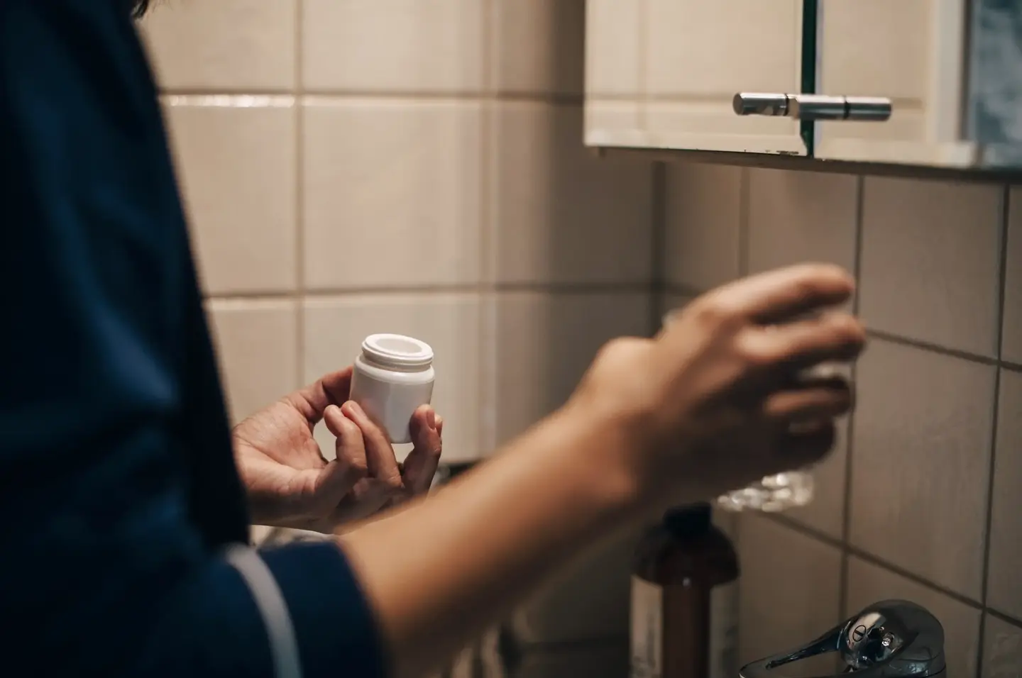 Närbild av händerna på en person som tar piller från badrumsskåpet.