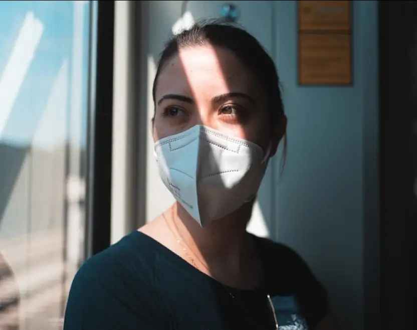 Kvinna med ansiktsmask tittar ut genom fönstret.