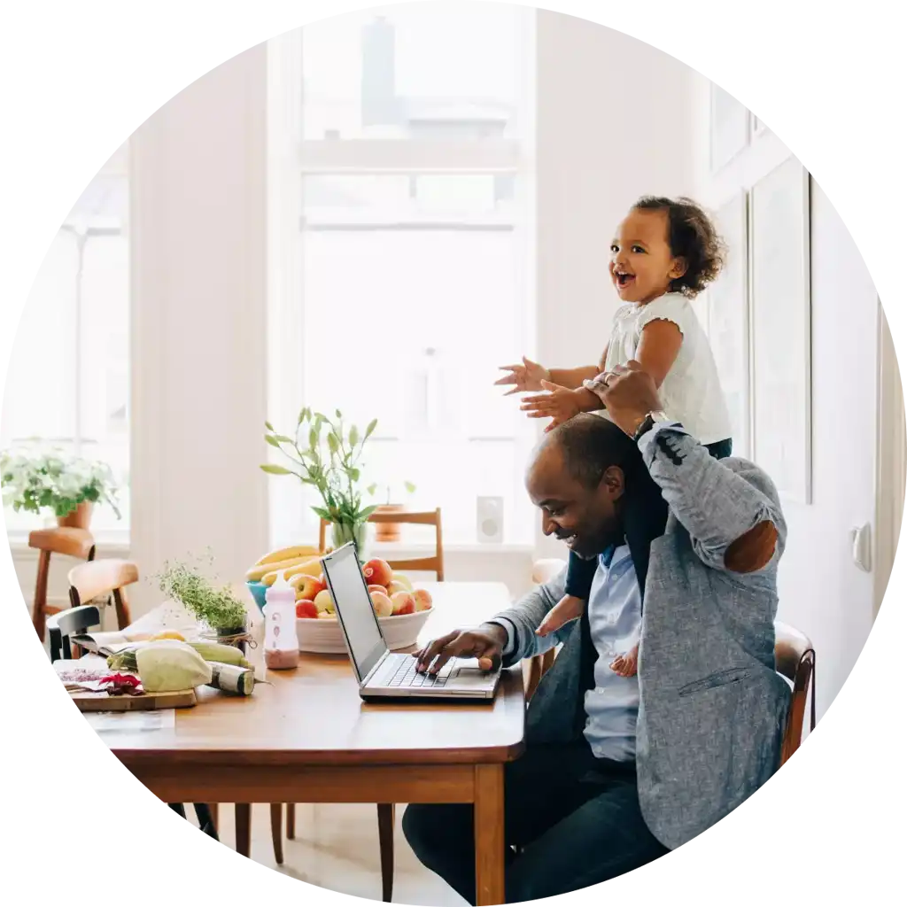 Pappa arbetar på laptop medan han leker med sitt barn på hemmakontoret.