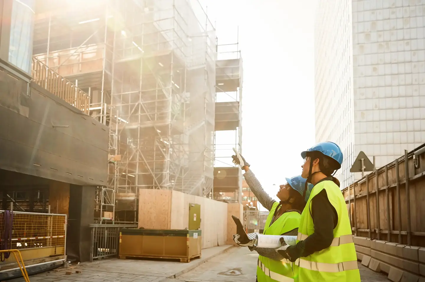 Två personer med hjälmar och reflexvästar inspekterar en ny byggnad under uppförande.