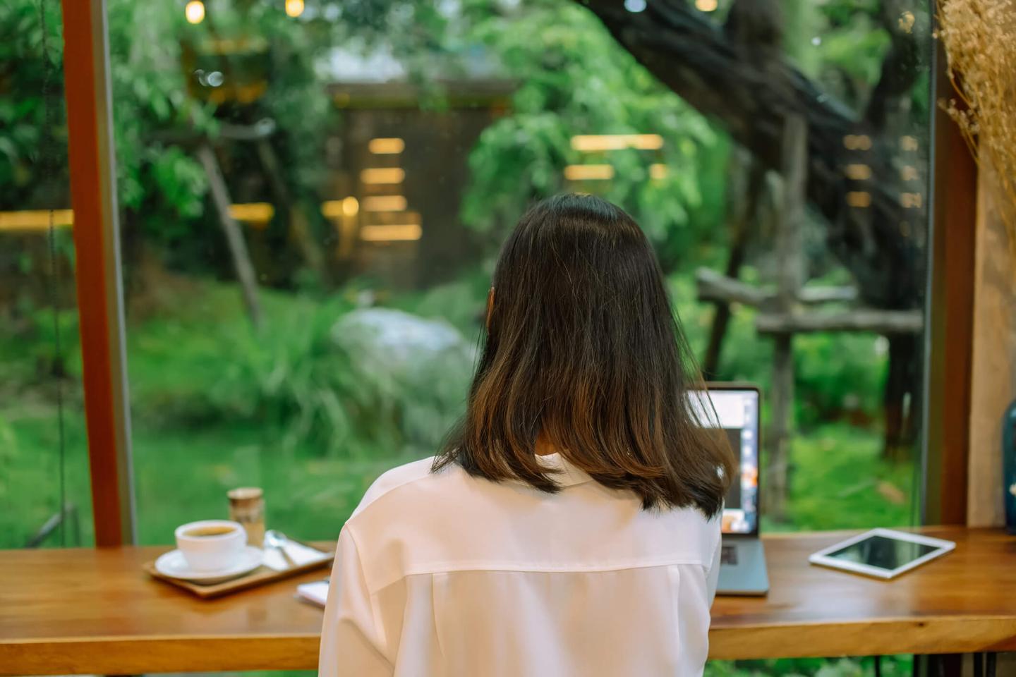 Ryggen på en kvinna som arbetar hemifrån, med utsikt över grön trädgård