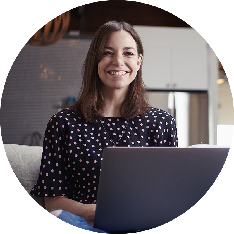 Glad kvinna som arbetar på sin laptop i soffan