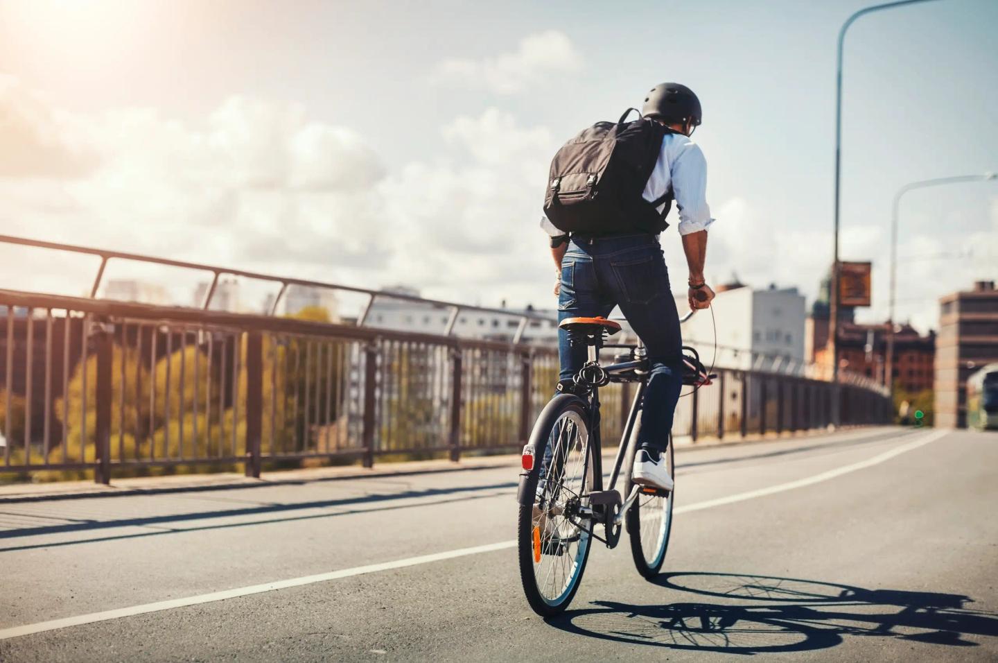 Personen cyklar över en betongbro med flerfamiljshus i bakgrunden.